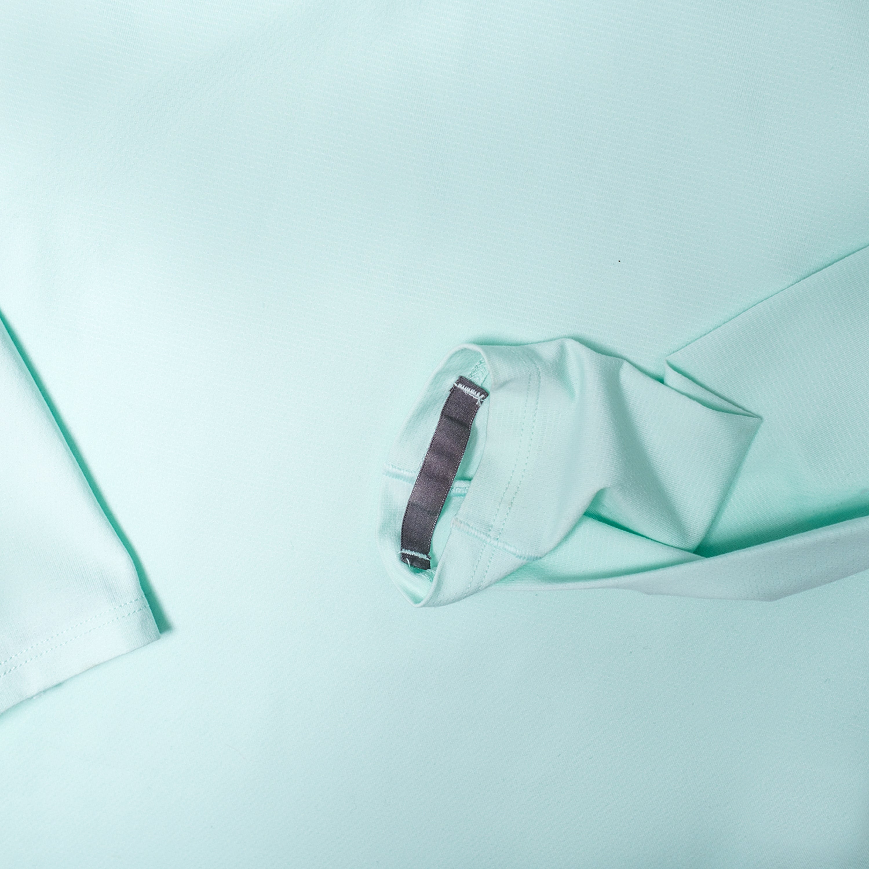 Close-up of a mint green garment sleeve with a grey thumb loop strap on the cuff.