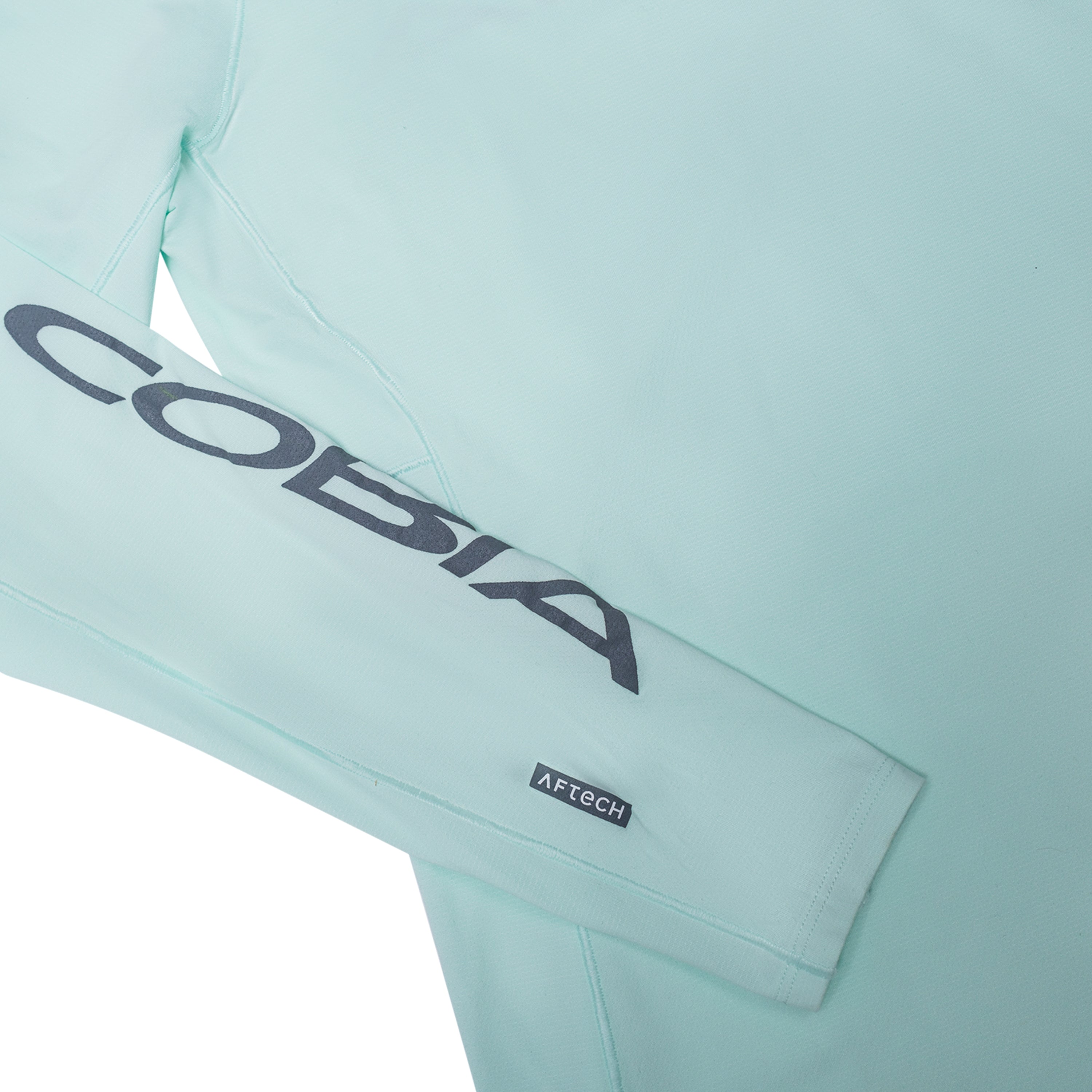 A light mint green long-sleeve shirt featuring the word 'COBIA' on the sleeve in grey.