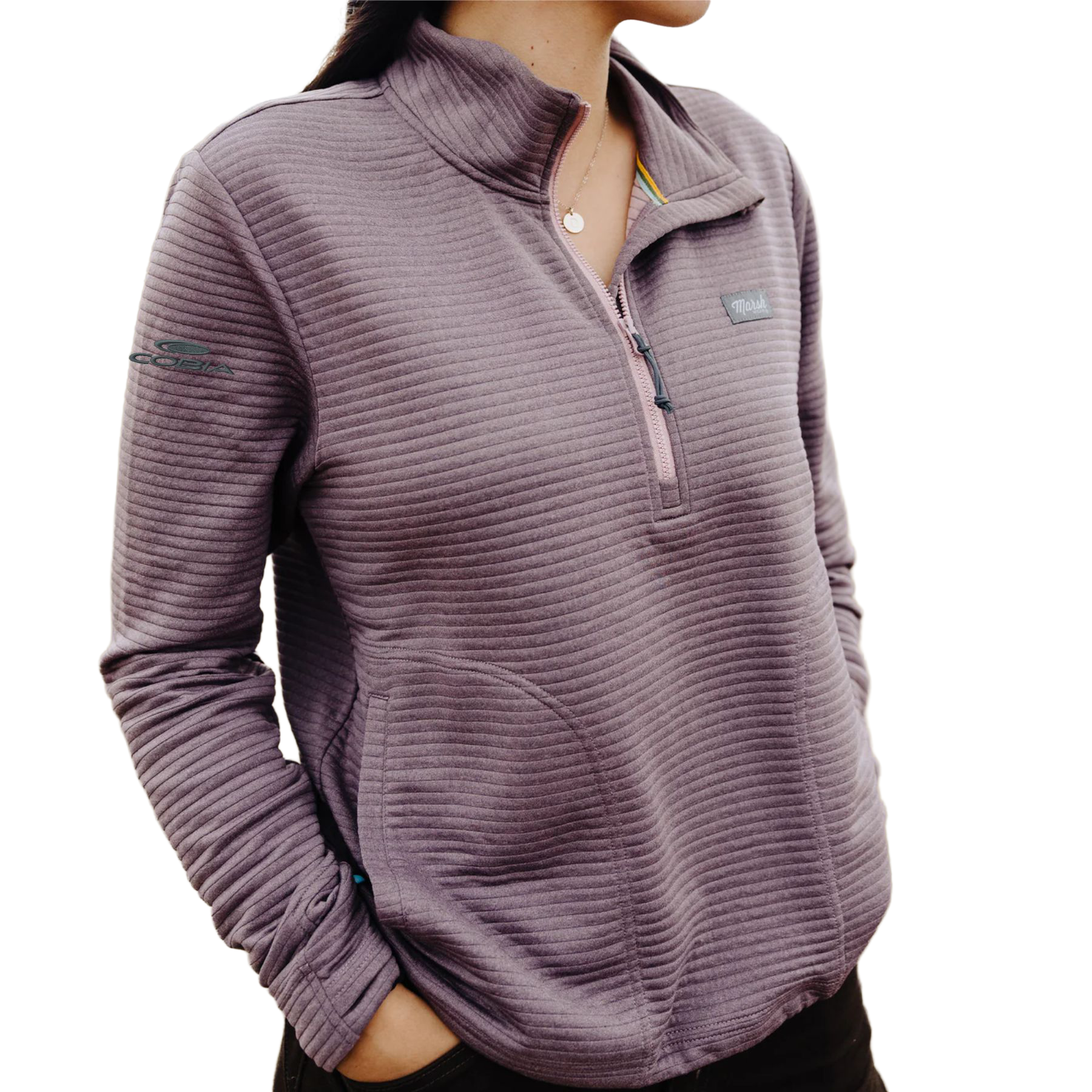 A woman wearing a ribbed, quarter-zip pullover sweatshirt in a dusty mauve-purple color. The sweatshirt features a stand-up collar, a partial zipper with a snap tab, a small rectangular logo patch on the left chest, and a small logo on the right sleeve.