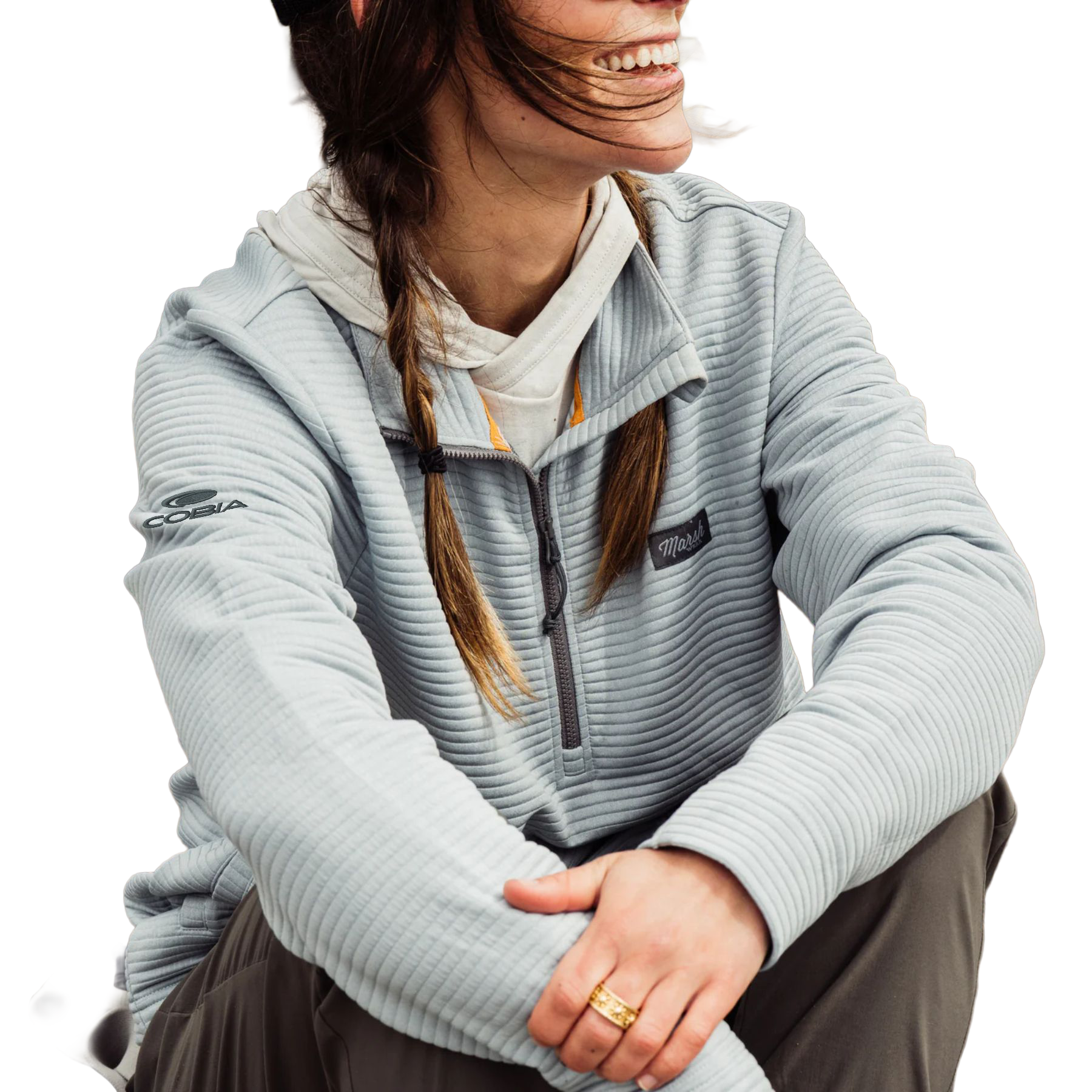 A woman wearing a light gray ribbed quarter-zip fleece pullover hoodie with a white inner hood with a logo on the sleeve shoulder.