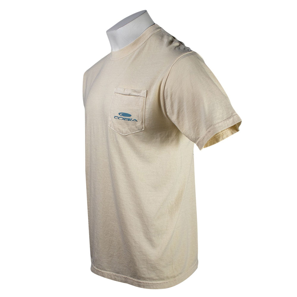 Side of a cream colored t-shirt with a blue cobia logo on the left chest pocket.