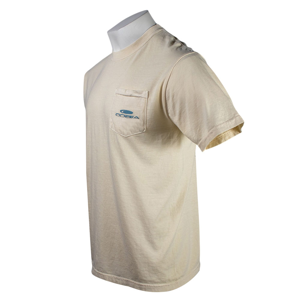 Side of a cream colored t-shirt with a blue cobia logo on the left chest pocket.