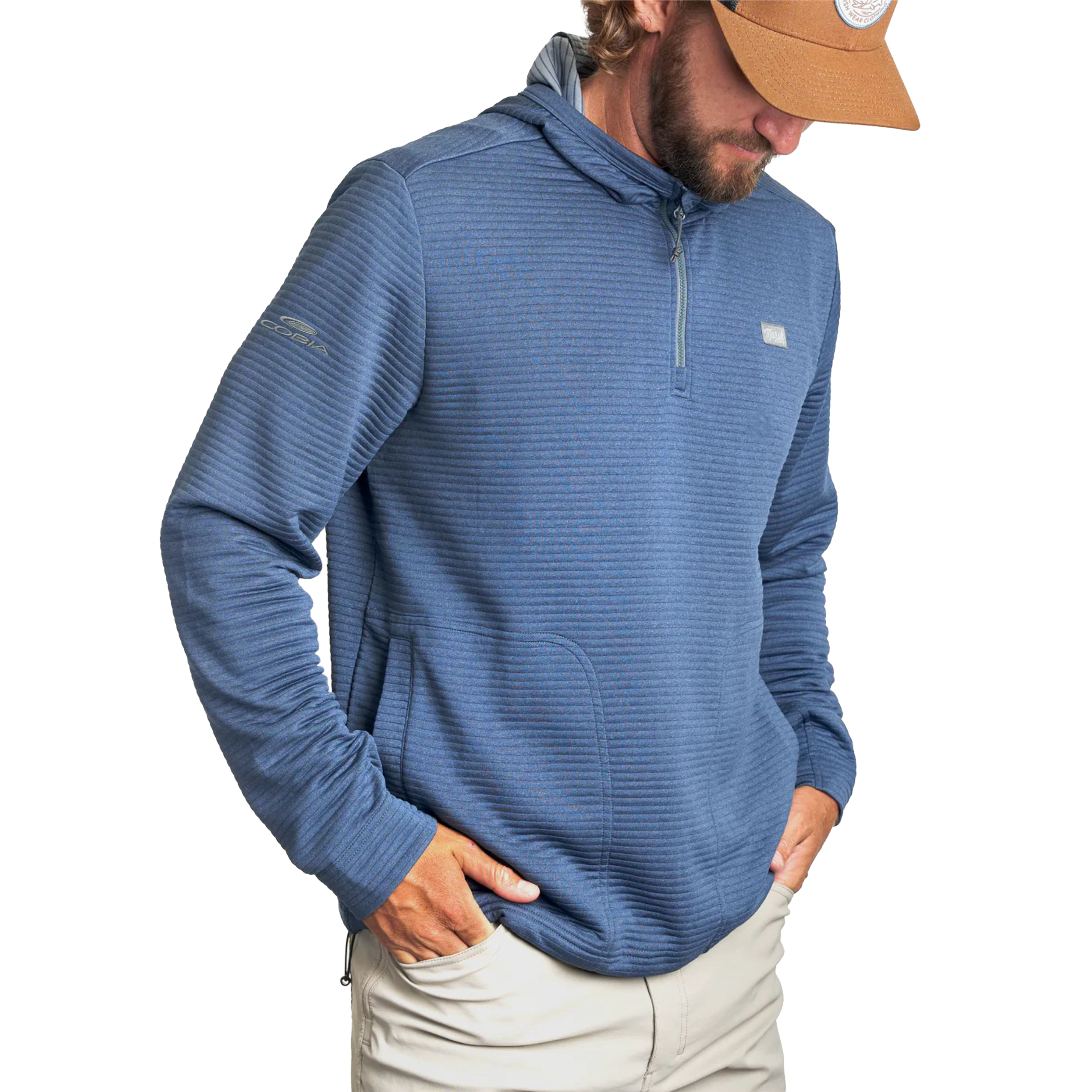 A man wearing a blue ribbed quarter-zip pullover hoodie with a kangaroo pocket, paired with light khaki pants and a tan baseball cap, shown against a plain white background.